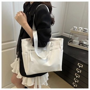 Detail of white corduroy tote bag with vertical texture and shoulder strap on a model