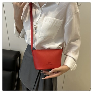 Détail du sac seau rouge avec texture grainée et logo DX sur une chemise blanche