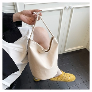 Detail of beige lychee texture bucket bag with metal chain charm and shoulder strap