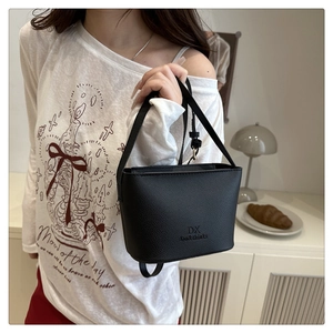 Détail du sac seau en cuir grainé noir avec logo de la marque et bandoulière réglable
