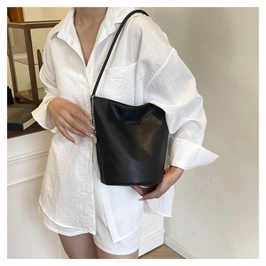 Detail of black pebbled leather bucket bag with silver chain on model in white shirt