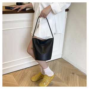 Side view of a black leather bucket bag with a metal chain charm on a fashion model