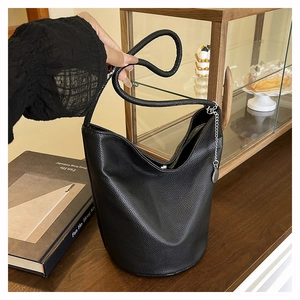 Detail of black lychee grain leather bucket bag with decorative metal chain and round tag