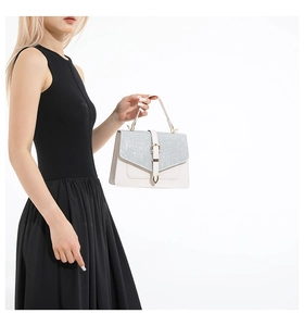 Details einer beige Lederhandtasche mit silbernem Glitzerüberschlag an einem schwarzen Kleid