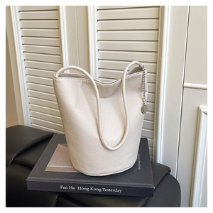 Close-up of soft beige leather bucket bag with pebble grain texture on a book