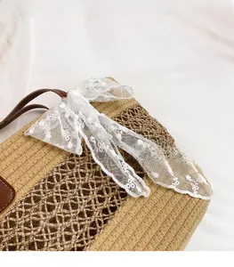 Close-up of woven straw tote bag with white lace bow detail and brown leather handle