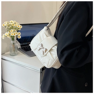 Close-up of white shoulder bag with silver bow buckle and pleated leather design