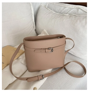 Close-up of beige bucket bag with adjustable strap and embossed detail on white bedding