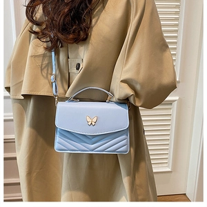 Detail of light blue quilted crossbody bag featuring golden butterfly clasp and V-shape stitching