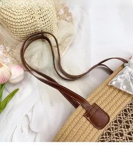 Detail of woven straw handbag with brown leather handles and decorative white lace bow