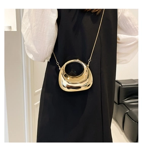 Detail of a metallic gold crescent bag with circular cutout and fine chain strap