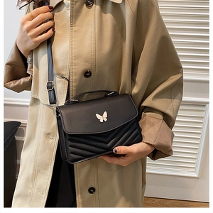 Detail of black chevron quilted crossbody bag featuring a metal butterfly clasp closure