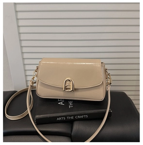 Détail d'un sac bandoulière beige avec une boucle métallique dorée en fer à cheval