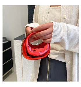 Close-up of metallic red crescent moon handbag with gold chain held against white knitwear