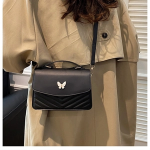 Detail of elegant black leather crossbody bag with V-shaped quilting and butterfly clasp