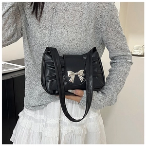 Detail of black pleated shoulder bag with silver metal bow worn by a model