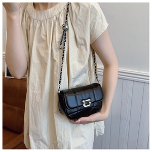 Detail of black quilted leather shoulder bag with silver metallic buckle and chain strap
