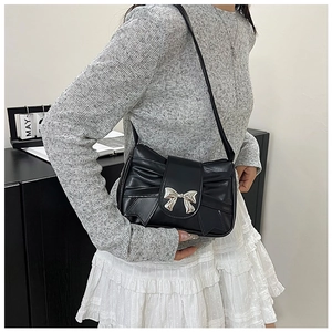 Detail of black pleated shoulder bag with a polished silver butterfly buckle on faux leather