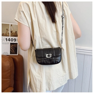 Detail of a black quilted saddle bag with silver C-shaped buckle on a model in a beige top