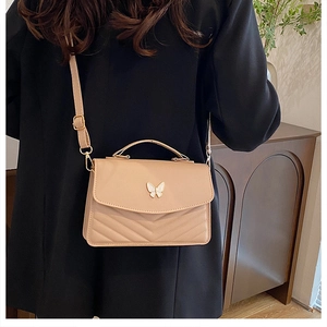 Detail of beige crossbody bag with V-shaped stitching and gold butterfly buckle on blazer