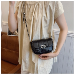 Detail of black quilted chain bag with silver buckle worn by a model in casual attire