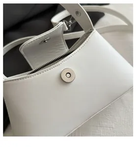 Detail of silver magnetic closure and zipper on white leather handbag with soft texture