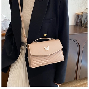 Detail of beige quilted crossbody bag featuring a delicate white butterfly metal clasp