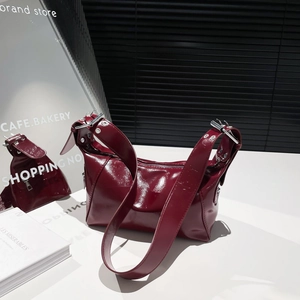 Deep red shiny patent leather shoulder bag with wide buckled strap and silver hardware