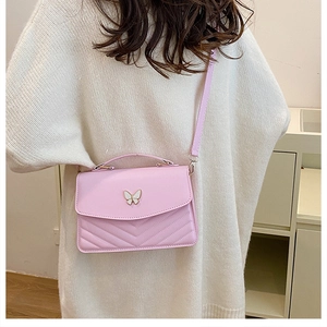 Close-up of pink quilted crossbody bag with golden butterfly logo worn by a model