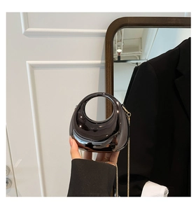 Close-up of black glossy crescent bag featuring circular handle and gold chain strap