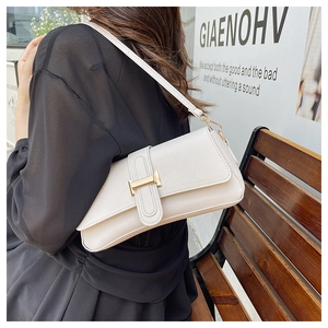 Close-up of white leather underarm bag featuring a golden H-shaped buckle and strap detail