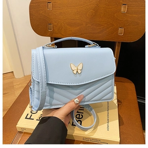 Detail of light blue quilted leather bag featuring a gold butterfly buckle on a yellow book