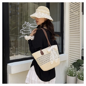 Detail of beige straw tote bag with white lace bow and brown leather handle on model