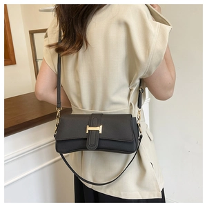 Close-up of black structured underarm bag with gold H-shaped clasp and Saffiano texture