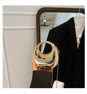 Close-up of a glossy gold crescent dumpling bag featuring round top handles and metal chain