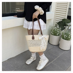 Detail of straw tote bag showing intricate hollow weave, brown handles and white lace bow