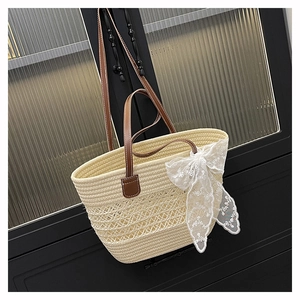 Detail of woven straw tote bag with brown leather handles and a delicate lace bow