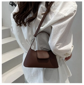 Détail d'un sac baguette en cuir marron avec logo embossé porté sur une chemise blanche