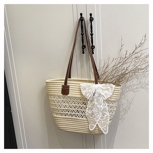Detail of hollow-woven beige straw tote with lace bow and brown leather strap