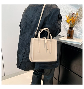 Sac à main beige chic porté sur un manteau noir avec des détails de pompons élégants