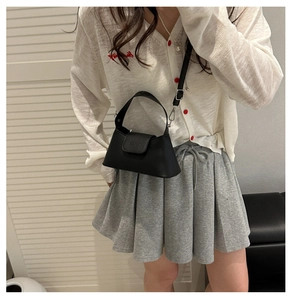 Detail of matte black leather baguette bag with silver hardware on a female model
