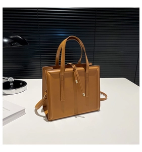 Détail d'un grand sac cabas carré marron en cuir lisse avec un nœud décoratif doré chic