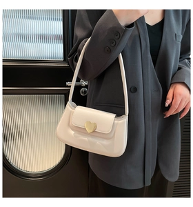 Close-up of cream shoulder bag featuring an elegant gold heart-shaped metal clasp