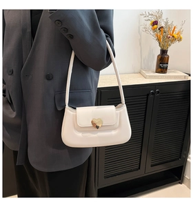 Sac sous le bras crème avec boucle coeur dorée présenté sur un mannequin élégant