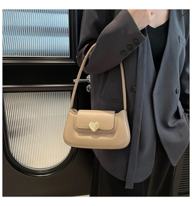 Détail d'un sac à bandoulière beige avec boucle métallique dorée en forme de cœur élégant