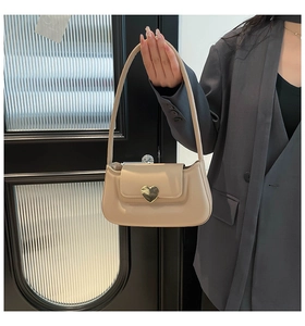 Détail d'un sac sous le bras en similicuir beige avec un fermoir cœur métallique