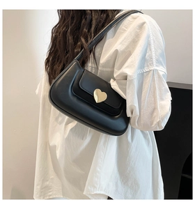 Detail of a black leather underarm bag featuring a gold heart buckle worn by a model