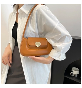 Close-up of caramel leather underarm bag with gold heart clasp on a white shirt