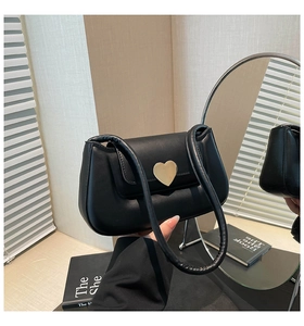 Détail d'un sac sous le bras noir avec boucle cœur dorée et bandoulière rembourrée
