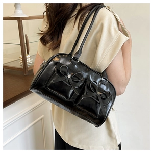 Side view of black glossy leather bow shoulder bag worn by model for daily commute